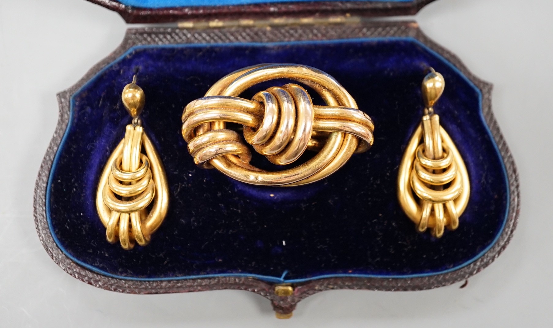 A cased Victorian yellow metal demi parure, comprising a brooch and pair of earrings of entwined knot form brooch width 43mm, gross weight 16.4 grams.